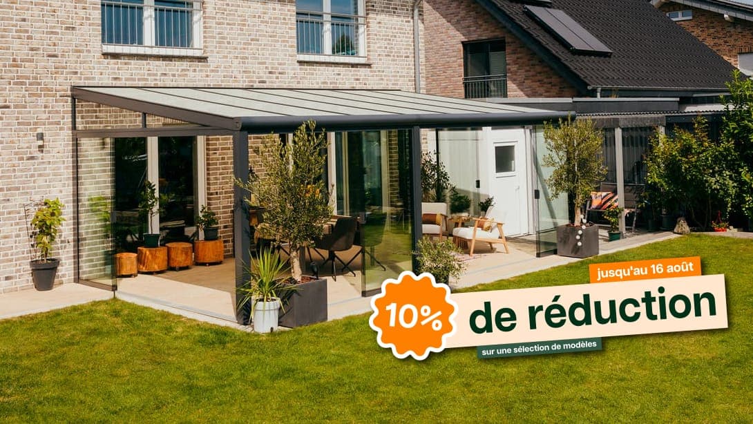 Terrasoverkapping aan een woning bij zonsondergang, met een stel dat ontspannen op een comfortabele bank zit.Véranda avec parois coulissantes en verre et éclairage d'ambiance