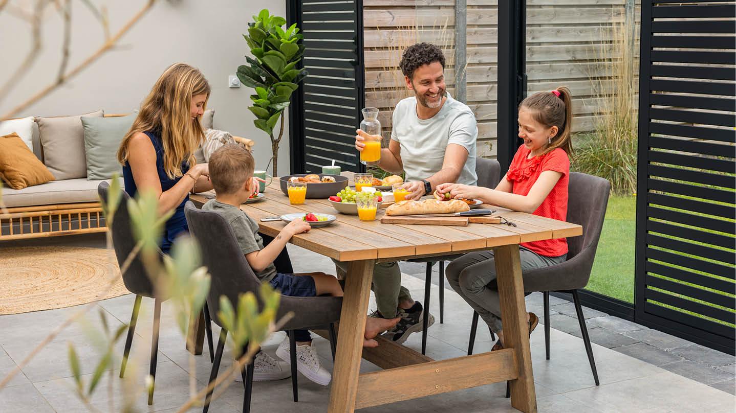Une famille souriante prend le petit-déjeuner sur une véranda Gumax® avec des panneaux d’ombrage